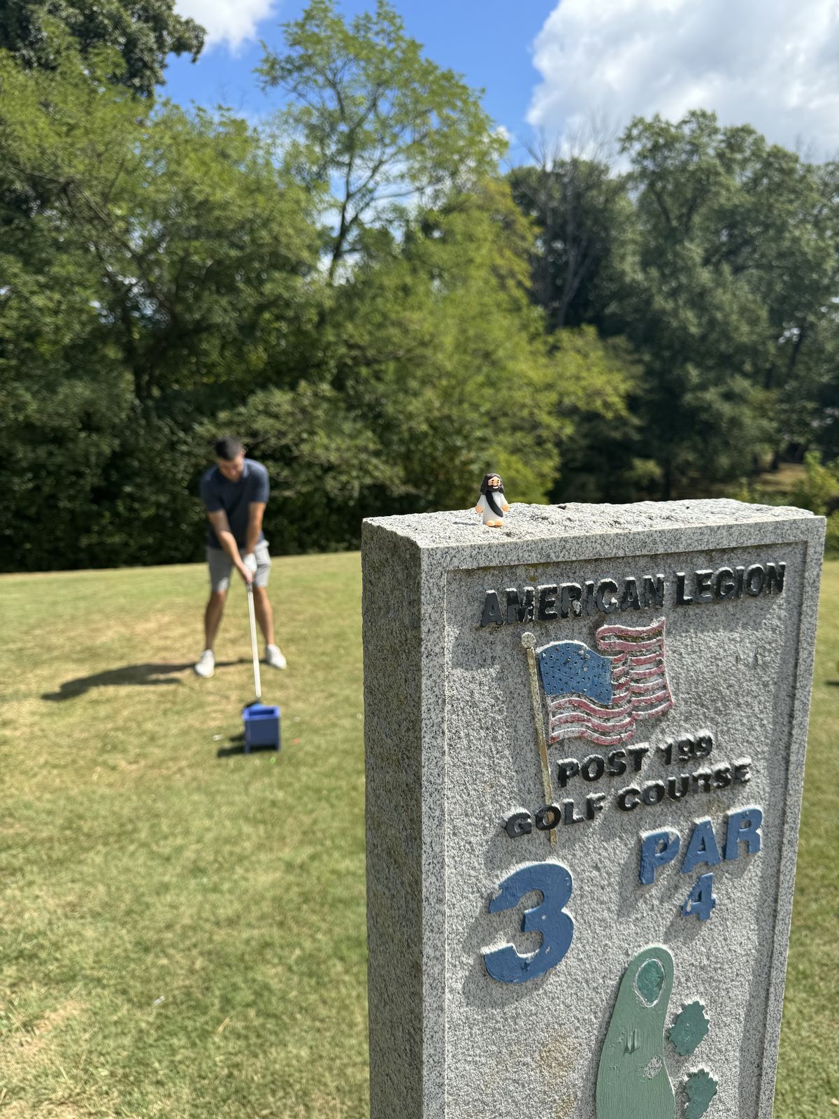 A golfer tees off beside the engraved American Legion Post 199 Golf Course marker at a past Aid for Adonai scramble in Edwardsville